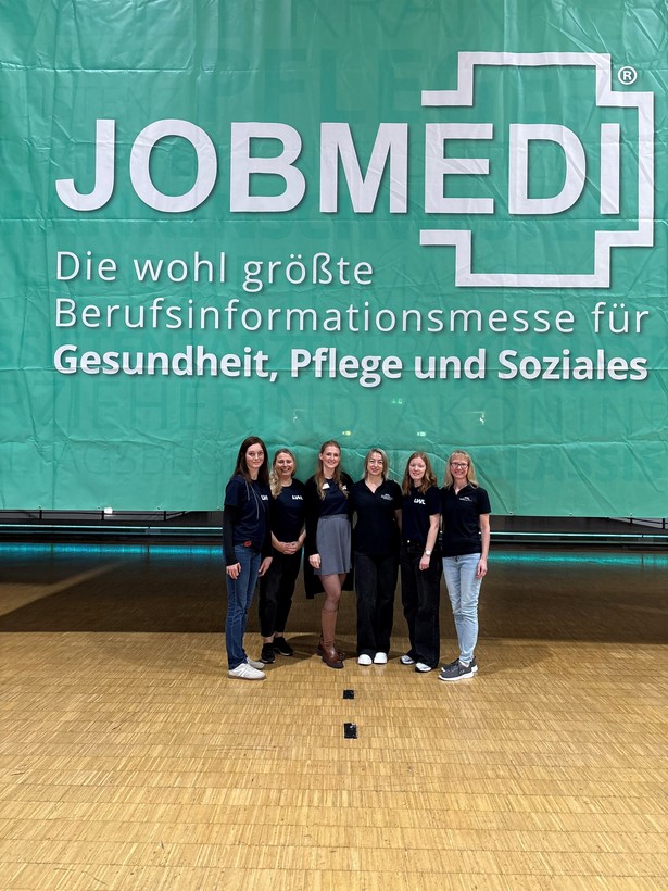 Sechs Personen stehen vor einem großen JOBMEDI-Banner auf einer Berufsinformationsmesse.