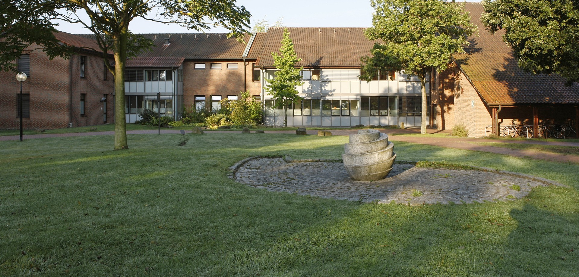 Mehrere Klinikgebäude mit einer grünen Wiese, einzelnen Bäumen rechts und links und Dekorsteinen davor platziert. (Bildquelle: LWL/Ritzenhoff)