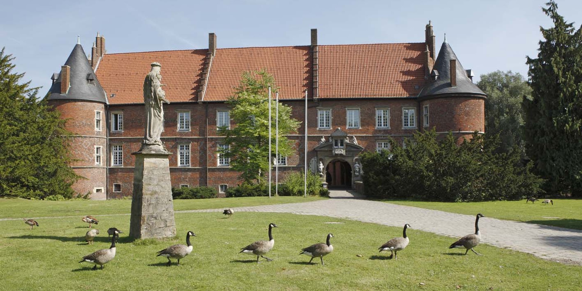 Vor dem Schloss der LWL-Klinik Herten laufen Gänse von links nach rechts durch das Bild.