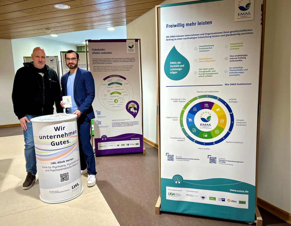 Zwei Personen stehen an einem Infostand mit Informationsplakaten.