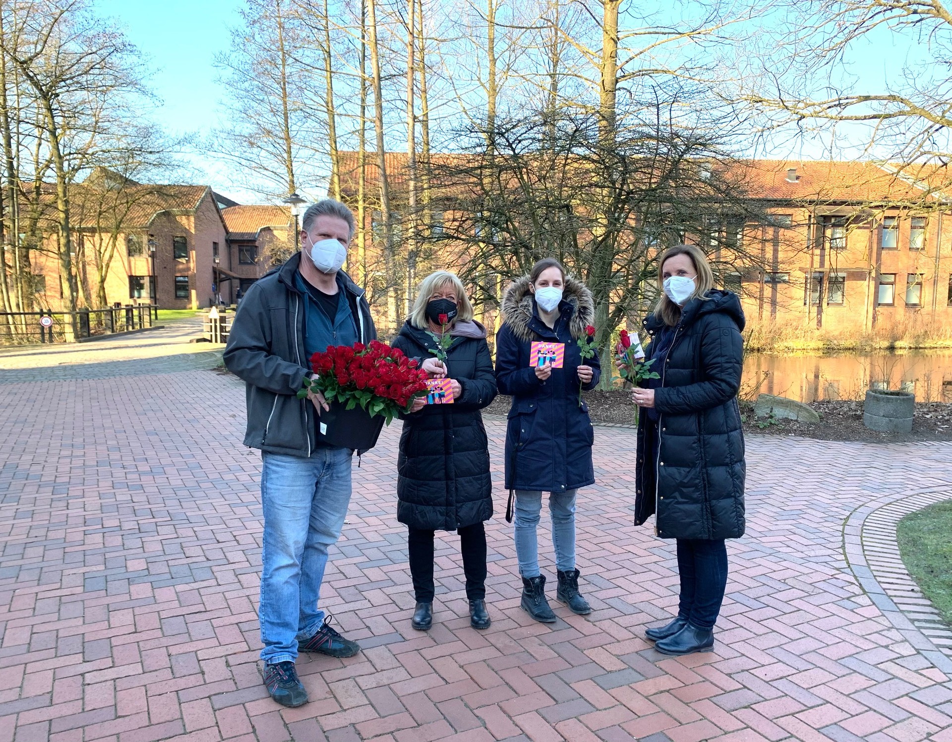 Eine Gruppe auf einem Klinikweg, links ein Mann mit vielen roten Rosen, rechts von ihm drei Frauen mit roter Rose und einer Dankeskarte in der Hand