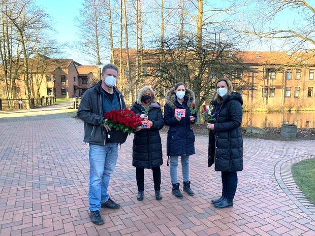 Eine Gruppe auf einem Klinikweg, links ein Mann mit vielen roten Rosen, rechts von ihm drei Frauen mit roter Rose und einer Dankeskarte in der Hand
