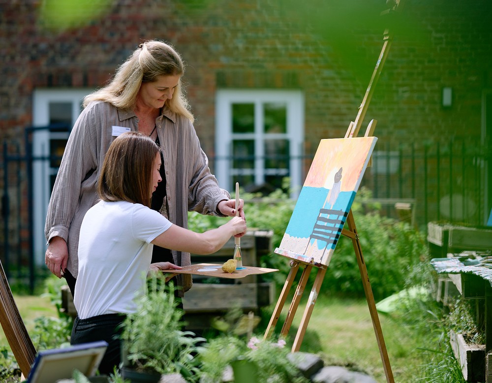 Zwei Frauen beim Malen an einer Staffelei im Garten.