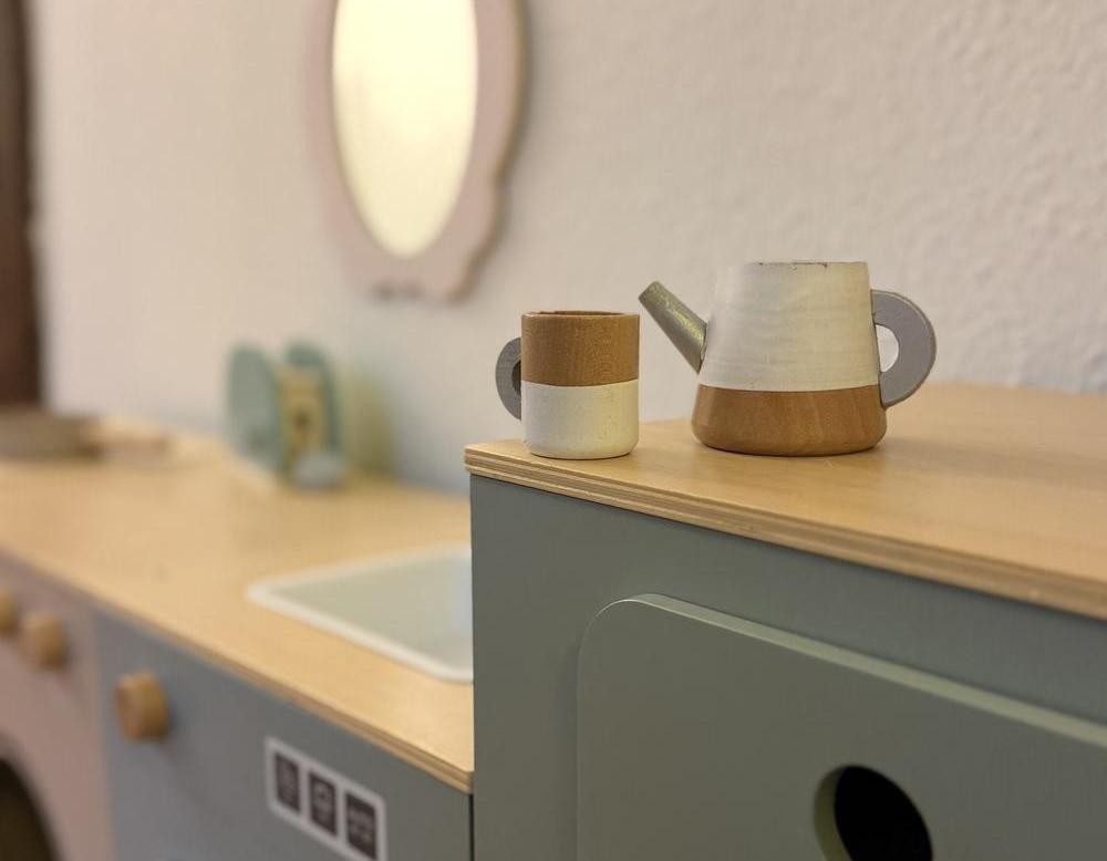 Kleines Spielküchenmöbel mit Holzbecher und Spielkanne auf einer Ablage