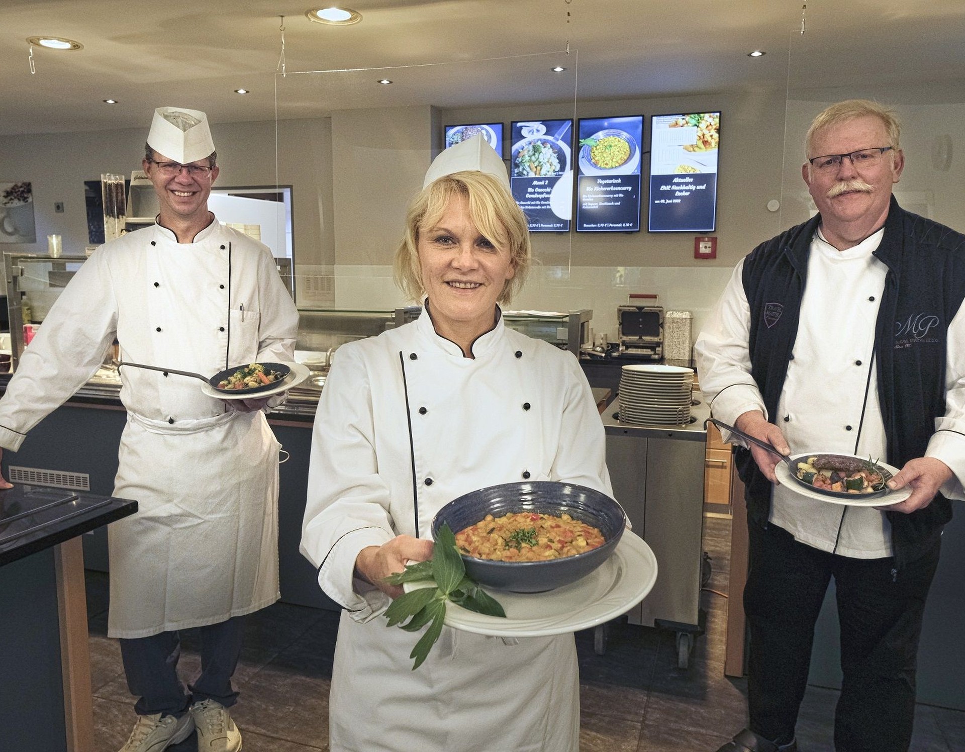 Drei Mitarbeitende der Küche präsentieren nachhaltige Gerichte in der Klinik-Kantine.