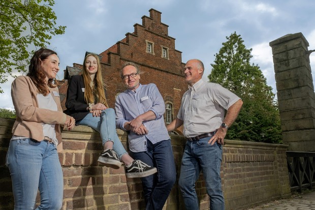 Vierköpfiges Team der Pflegedirektion mit zwei Frauen und zwei Männern sitzen auf oder lehnen an der Mauer einer historischen Schlossbrücke. Vierköpfiges Team der Pflegedirektion mit zwei Frauen und zwei Männern sitzen auf oder lehnen an der Mauer einer historischen Schlossbrücke.