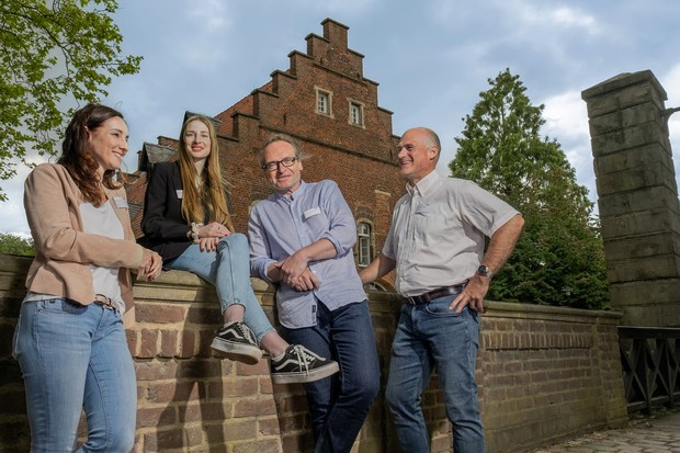 Vierköpfiges Team der Pflegedirektion mit zwei Frauen und zwei Männern sitzen auf oder lehnen an der Mauer einer historischen Schlossbrücke.