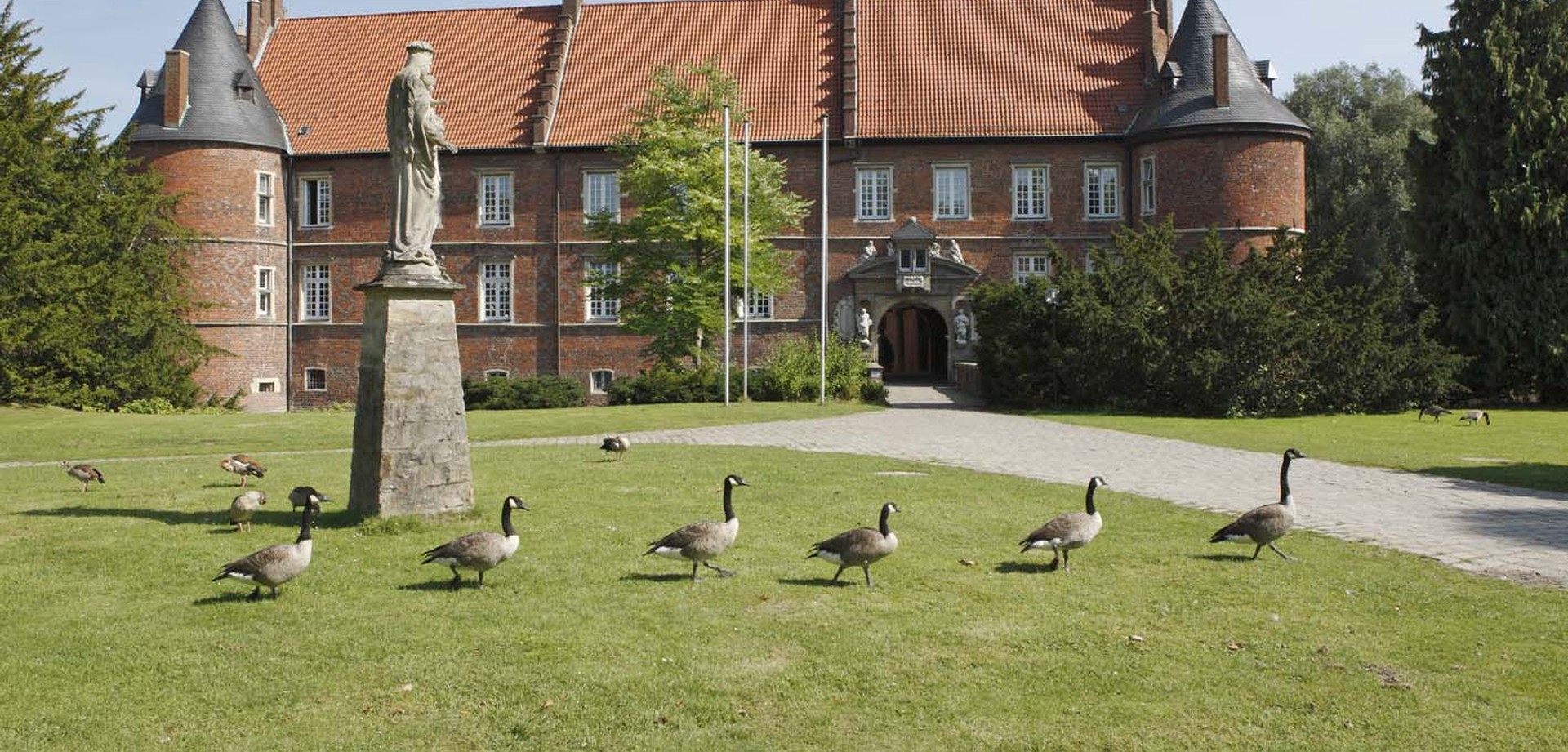 Das Schloss der LWL-Klinik Herten bei Sonnenschein und mit Kanadagänsen im Vordergrund auf der Wiese. Bildquelle: LWL/Ritzenhoff