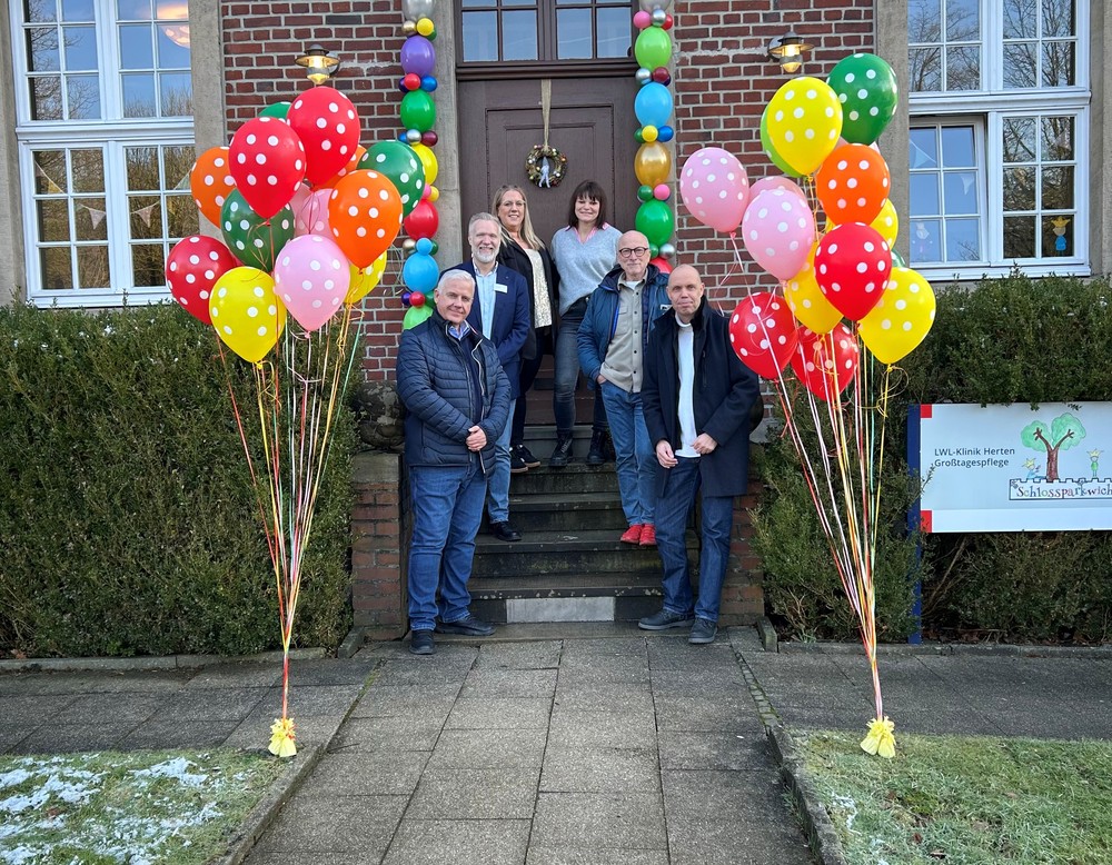 Gruppe von Personen vor einem Gebäude mit bunten Luftballons