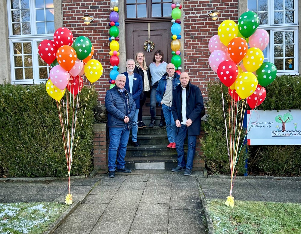 Mitarbeitende vor dem Eingang der Großtagespflege Schlossparkwichtel, geschmückt mit bunten Luftballons.
