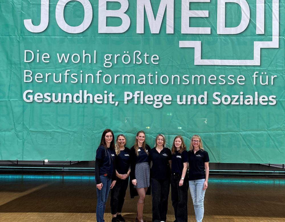 Sechs Personen stehen vor einem großen JOBMEDI-Banner auf einer Berufsinformationsmesse.