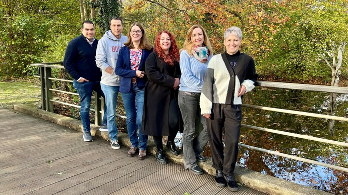 Sechs Personen stehen auf einer Brücke vor herbstlicher Natur und blicken in die Kamera.