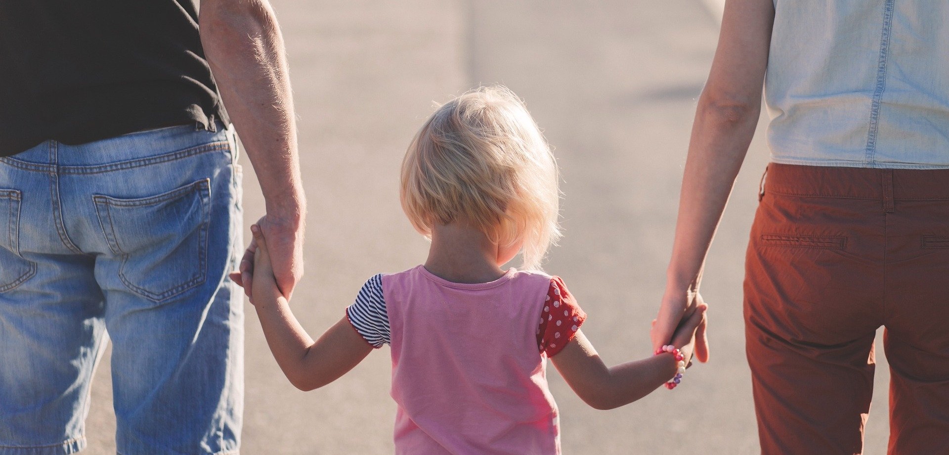 Mutter und Vater halten ihre Tochter an den Händen, das Kind ist in der Mitte zwischen den beiden