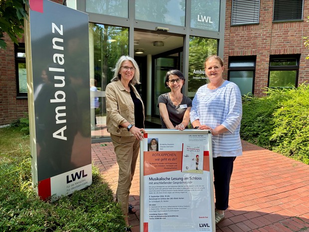 Drei Frauen vor dem Eingang der LWL-Klinik Herten mit einem Veranstaltungsplakat.