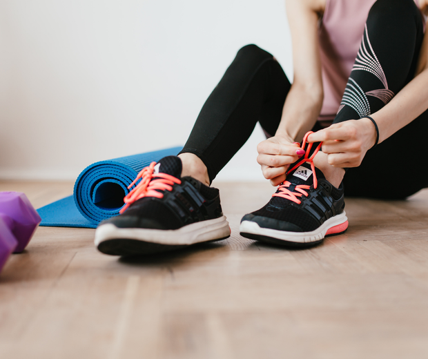 Eine sitzende Person, welche sich die Schuhe zubindet, neben der Person ist eine Yogamatte (Bildquelle:Canva) Eine sitzende Person, welche sich die Schuhe zubindet, neben der Person ist eine Yogamatte (Bildquelle:Canva)