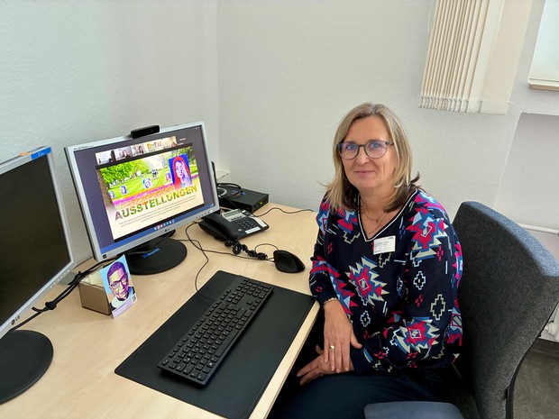 Eine Frau sitzt an einem Schreibtisch vor einem Computer mit geöffneter Präsentation.