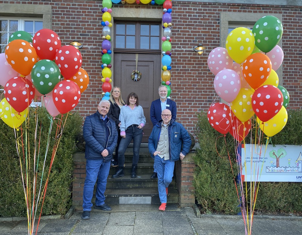 Gruppe von Personen vor einem Gebäude mit bunten Luftballons