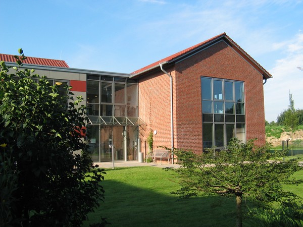 Das Gebäude der Tagesklinik in Dorsten aus roten Ziegelsteinen mit großen Fenstern, Wiese und Gebüsch links und rechts. Bildquelle: LWL/Ritzenhoff